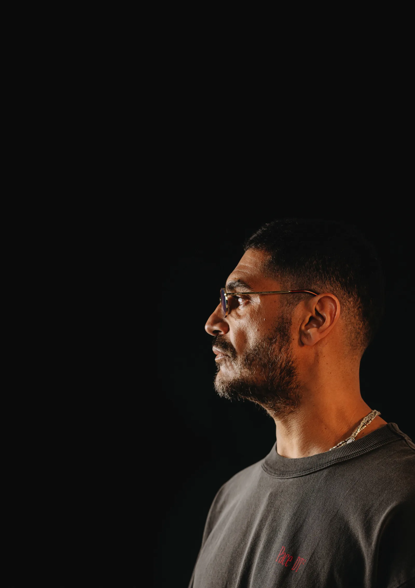 Retrato de Criolo de perfil, camiseta cinza, fundo preto