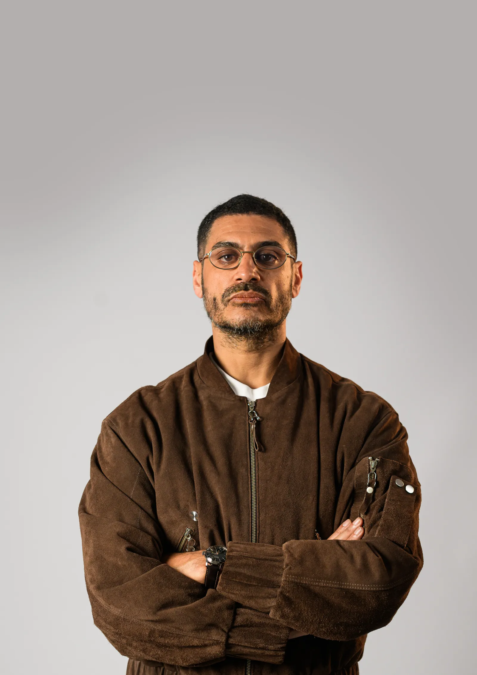 Criolo em pé, braços cruzados, jaqueta marrom
