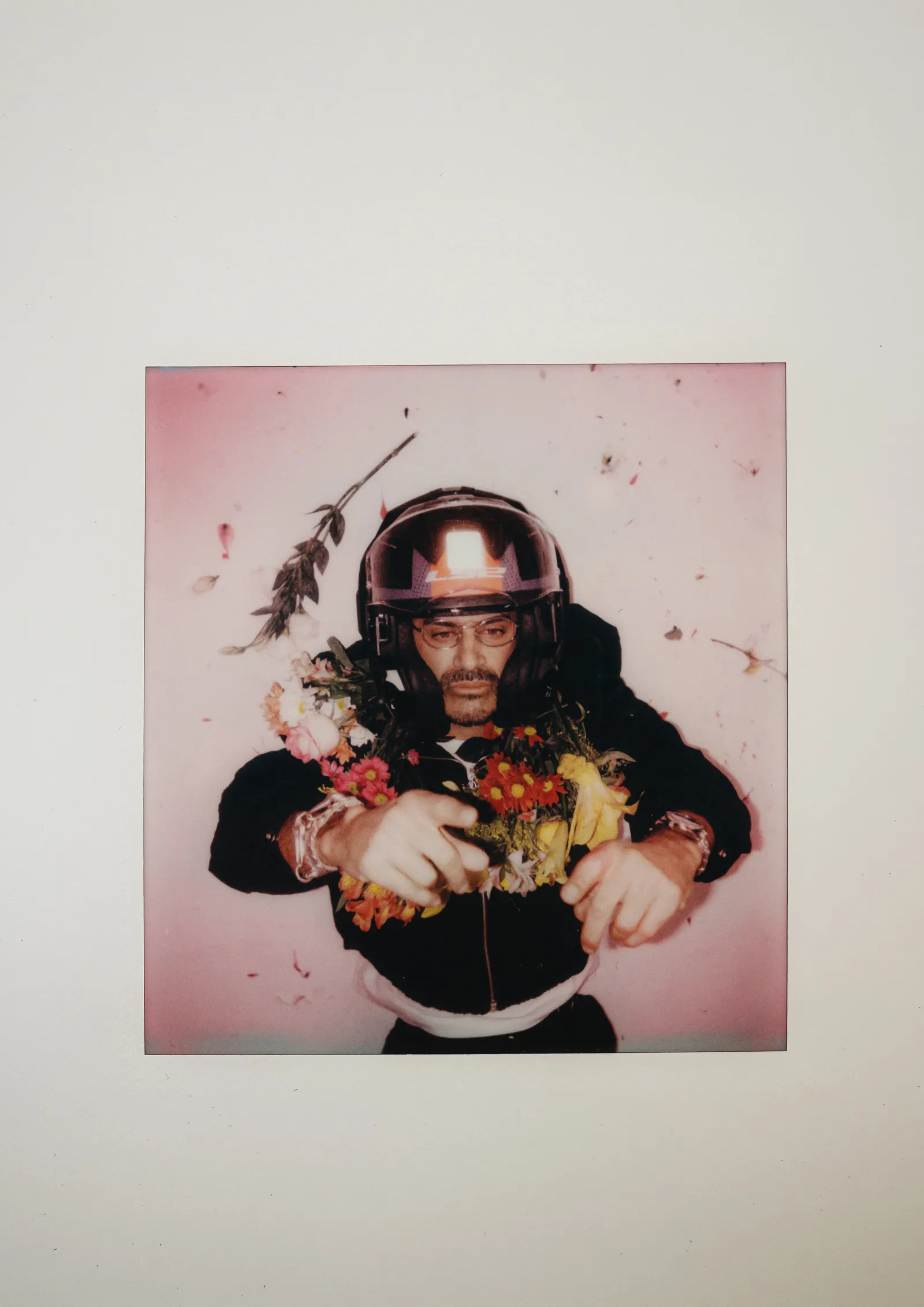 Polaroid de Criolo com capacete e flores presa em uma parede branca